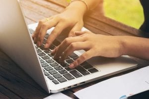 Woman's hand typing on a laptop adding holiday hours online.