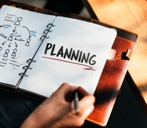 Woman writing "planning" in notebook for her digital marketing plan.